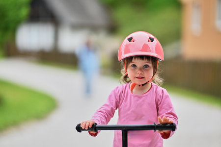 A little girl, dressed in a cute outfit and wearing a helmet, excitedly learning to ride her bike for the first time, filled with joy and determination.の写真素材