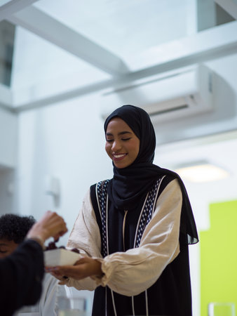 A woman in a hijab extends a platter of dates to her diverse family, creating a scene of unity and joy as they come together to break their fast during the holy month of Ramadan, symbolizing the shared love and spiritual connection within their cultural and religious traditionsの写真素材