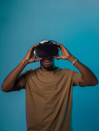 In a futuristic visual, an African American man stands isolated against a striking blue backdrop, adorned with VR glasses that transport him into a cutting-edge virtual reality experience, merging technology and innovation in a contemporary displayの写真素材