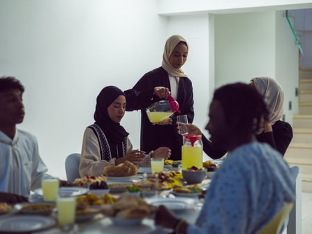 A diverse Islamic family gathers for iftar, joyfully breaking their fast together during Ramadan, with a Muslim woman in a beautiful hijab gracefully pouring water to mark the end of their fast, showcasing the unity, love, and spiritual connection that define this special family momentの写真素材
