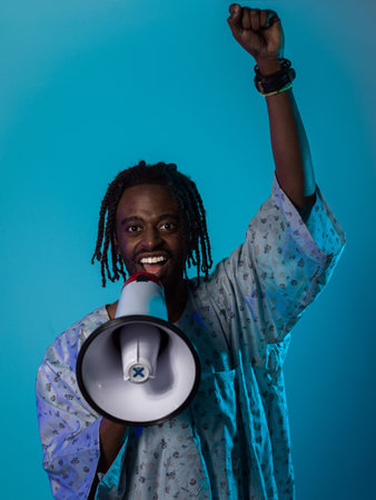 In a powerful and symbolic image, an African American man wears traditional clothing, passionately wields a megaphone against a striking blue background, with his hand raised in the air symbolizing his vocal and cultural empowerment in the pursuit of social justice and equalityの写真素材