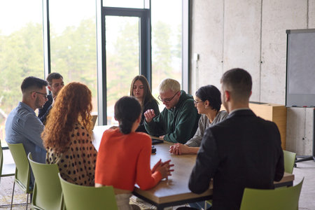 A young, diverse business team sitting together in a modern office, exchanging ideas and business...