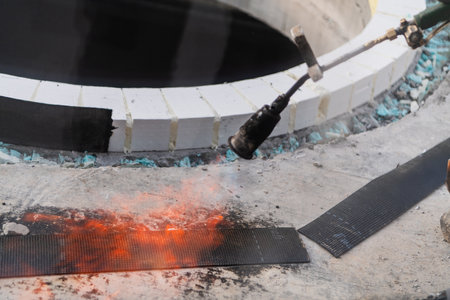 An industrial worker uses fire to soften a rubber underlay for floor insulation, showcasing precision and skill in a critical step of the construction processの写真素材