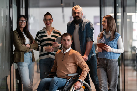 A businessman with disability in a wheelchair is surrounded by supportive colleagues in a modern office, showcasing the strength of teamwork, inclusivity, and empowerment in the face of challenges.の写真素材