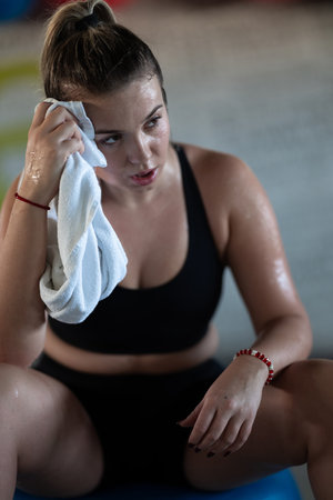A beautiful and fit woman sitting on a gym ball with a towel, resting and recovering after an intense workout.の写真素材