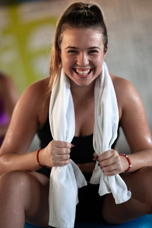A beautiful and fit woman sitting on a gym ball with a towel, resting and recovering after an intense workout.の写真素材