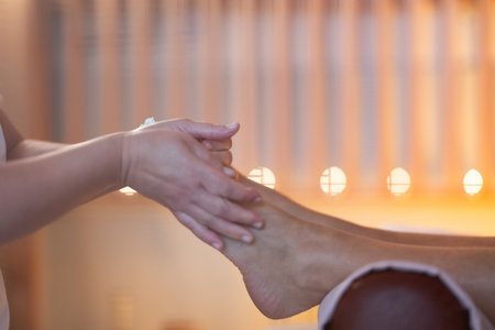Foot Massage Therapy in a Relaxing Spa Setting. A professional massage therapist in a white uniform provides a soothing foot massage to a client in a calm and serene spa environmentの写真素材