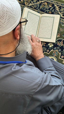 Mecca, Saudi Arabia - May 2, 2024: Young man, Hajj and Umrah pilgrim sitting and reading Quran in...