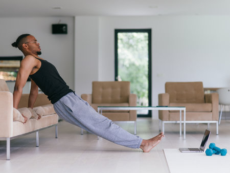 Training At Home. Sporty man doing the training while watching an online tutorial on a laptop, exercising in the living room, free space.の写真素材