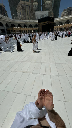 A bald man poses for a photo in front of the Kaaba at noon after performing Umrah at Masjid al-Haram, Mecca. A sacred Islamic pilgrimage in the heart of the holy mosque under the bright sunlight.の写真素材