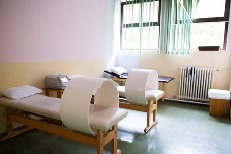 A well-lit physiotherapy treatment room featuring specialized medical equipment, therapy beds, and a comfortable clinical setting. The room has a clean and organized appearance with natural light from large windowsの写真素材