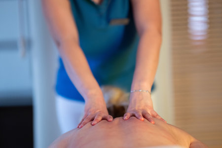 Relaxing Back Massage in a Spa Setting. A professional massage therapist in a blue uniform provides a relaxing back massage to a client lying on a massage table.の写真素材