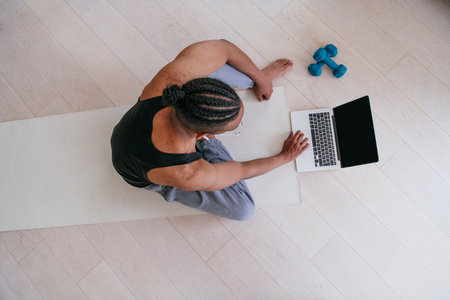 Training At Home. Sporty man doing the training while watching an online tutorial on a laptop, exercising in the living room, free space.の写真素材