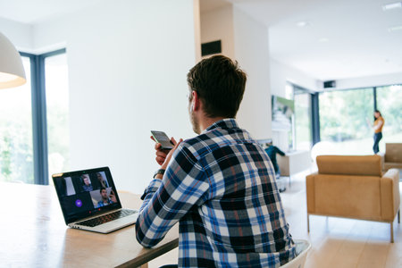 A freelancer sitting at a table in a modern living room, with headphones using a laptop for business video chat, conversation with friends and entertainmentの写真素材