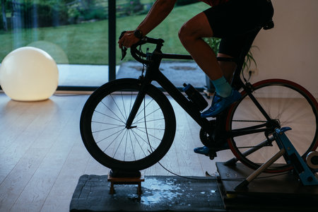 A triathlete riding a triathlon bike on a machine simulation in a modern living room. Training during pandemic conditions.の写真素材
