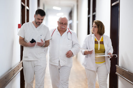 A group of healthcare professionals in white uniforms walking through a hospital hallway while reviewing patient documents and discussing treatment plans.の写真素材