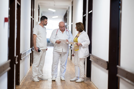 A group of healthcare professionals in white uniforms walking through a hospital hallway while reviewing patient documents and discussing treatment plans.の写真素材
