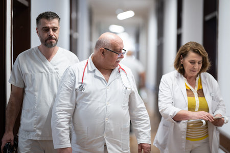 A group of healthcare professionals in white uniforms walking through a hospital hallway while reviewing patient documents and discussing treatment plans.の写真素材