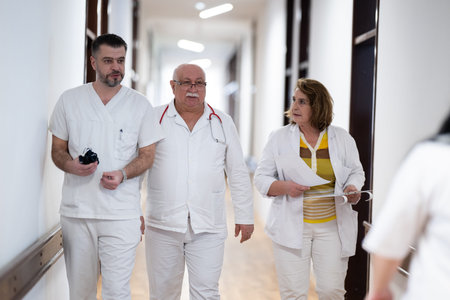 A group of healthcare professionals in white uniforms walking through a hospital hallway while reviewing patient documents and discussing treatment plans.の写真素材