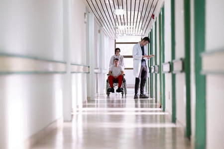 Young Male Patient in Wheelchair Assisted by Female Medical Professionalの写真素材