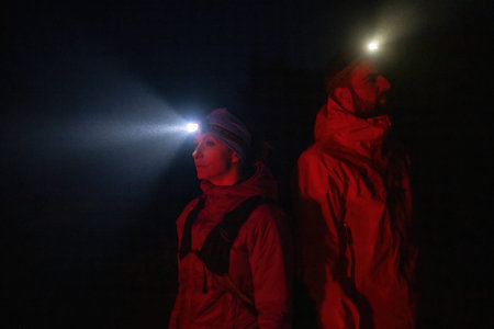 Exploring the Night Forest.Couple equipped with headlamps explore a forest in total darkness, with beams of light cutting through the night air.の写真素材