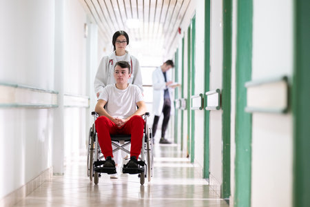 Young Male Patient in Wheelchair Assisted by Female Medical Professionalの写真素材