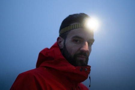 Balancing on the Mountain Trail at Dusk.A lone hiker balances on a rocky mountain trail during early morning or dusk, with a headlamp lighting the misty path.の写真素材