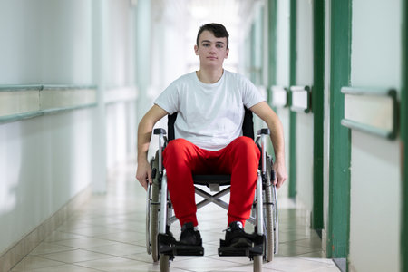 Young teenage boy smiling while sitting in a wheelchair in a hospital hallway. Rehabilitation and positivity concept.の写真素材