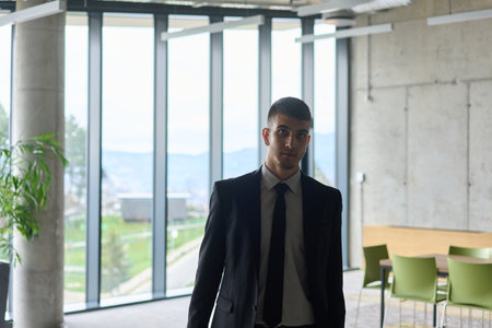A determined businessman in a black suit confidently walks through the office, embodying professionalism and focus as he heads towards new challengesの写真素材