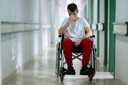 Sad Young Man in Wheelchair.Teenage boy sitting in wheelchair with sad expression in hospital hallway. Emotion and struggle in recovery.の写真素材