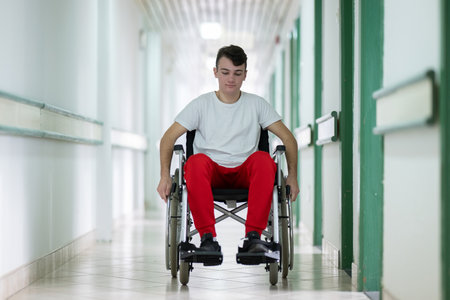 Young teenage boy smiling while sitting in a wheelchair in a hospital hallway. Rehabilitation and positivity concept.の写真素材