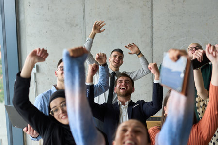 A diverse team of business professionals ecstatically celebrating their success in a modern office, expressing triumph and unity after achieving their goalsの写真素材