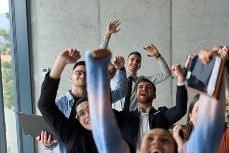 A diverse team of business professionals ecstatically celebrating their success in a modern office, expressing triumph and unity after achieving their goalsの写真素材