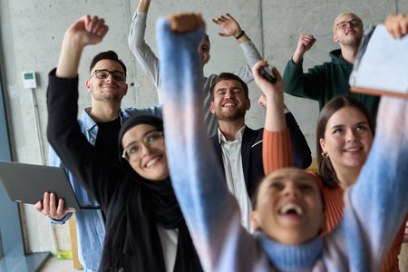 A diverse team of business professionals ecstatically celebrating their success in a modern office,...