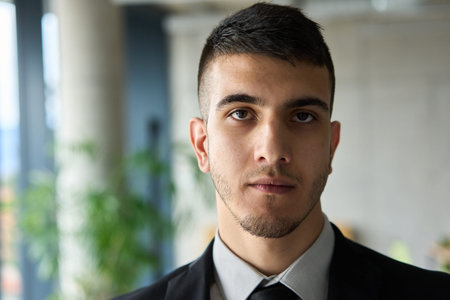 A close up portrait of a company director in a black suit, standing confidently in a modern office, exuding leadership, professionalism, and authority.の写真素材