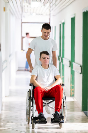 Young Male Patient in Wheelchair Assisted by Female Medical Professionalの写真素材