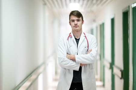 Doctor Standing in Hospital Hallway.Young male doctor standing confidently in a hospital corridor with a stethoscope. Medical professionalism concept.の写真素材
