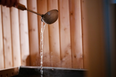Sauna Bucket and Towels Close Up.Detailed close up of sauna bucket with ladle and essential oils next to rolled towels on wooden bench inside sauna.の写真素材