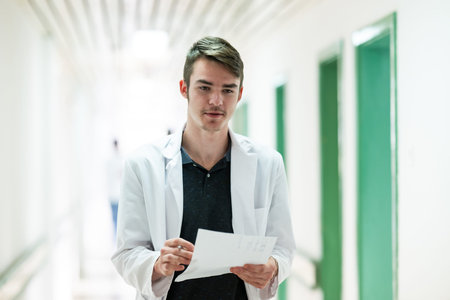 Doctor Reading Documents in Hospital.Young male doctor walking in hospital hallway while reading...