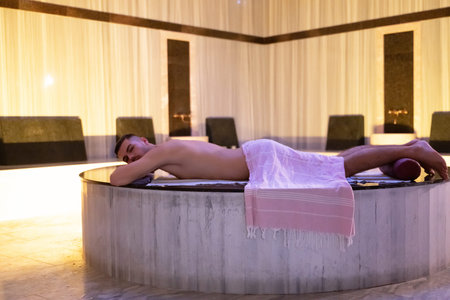 Man relaxing on a marble platform inside a Turkish bath with warm lighting.の写真素材