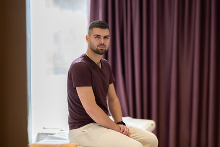 A man sitting calmly on a treatment table, waiting for a physical therapy session in a clinic environment.の写真素材