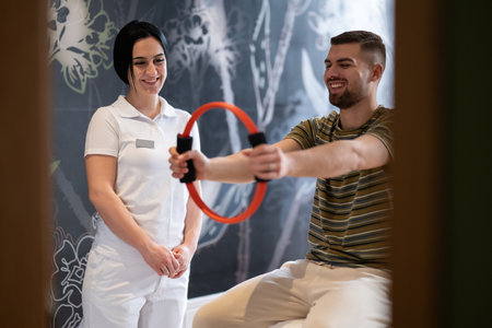 Physical Therapy Session with Resistance Ring.A male patient performing arm exercises using a resistance ring under supervision during a rehabilitation session.の写真素材
