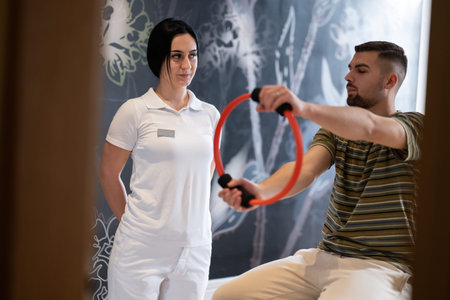 Physical Therapy Session with Resistance Ring.A male patient performing arm exercises using a resistance ring under supervision during a rehabilitation session.の写真素材