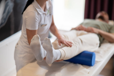 Physiotherapy Session with Blue Foam Roller.A therapist guiding a patient through leg exercises with the help of a blue foam roller in a therapy clinic.の写真素材