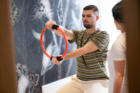 Physical Therapy Session with Resistance Ring.A male patient performing arm exercises using a resistance ring under supervision during a rehabilitation session.の写真素材