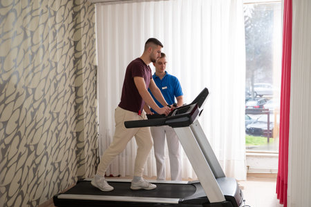 Physical Therapy on Treadmill.Man undergoing physical therapy with trainer assistance on a treadmill indoors.の写真素材
