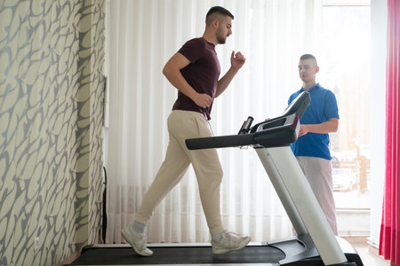 Physical Therapy on Treadmill.Man undergoing physical therapy with trainer assistance on a treadmill indoors.の写真素材