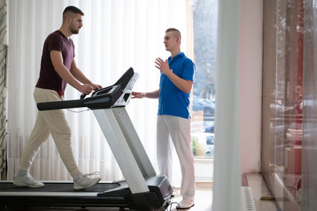 Physical Therapy on Treadmill.Man undergoing physical therapy with trainer assistance on a treadmill indoors.の写真素材