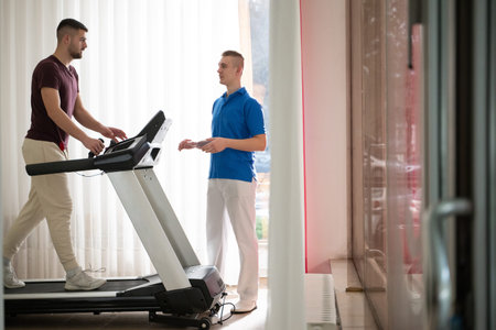 Physical Therapy on Treadmill.Man undergoing physical therapy with trainer assistance on a treadmill indoors.の写真素材