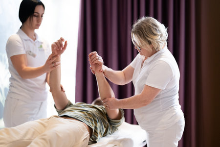 Two therapists assist a male patient in a physiotherapy session, focusing on arm rehabilitation exercises.の写真素材